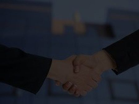 Two people shaking hands in front of a building.